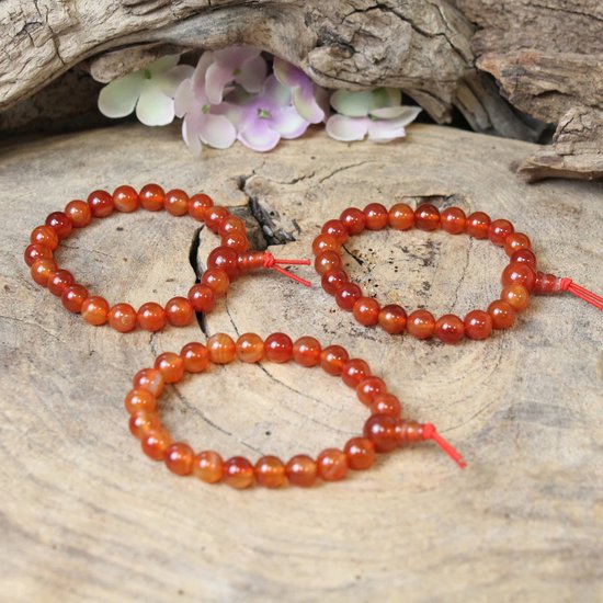 Drie armbanden van oranje carneool kralen met rode draden, op hout