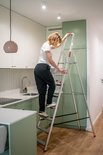 Vrouw klimt op de aluminium huishoudladder in een keuken.