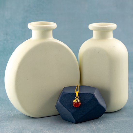 Gouden ketting met oranje steen op donkerblauwe steen tussen twee lichte vazen.