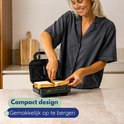 Vrouw plaatst broodjes in een zwart tosti-apparaat. Compact design.