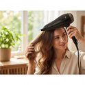 Vrouw met lang bruin haar, droogt haar haar met een zwarte Lafe haardroger in een lichte badkamer.