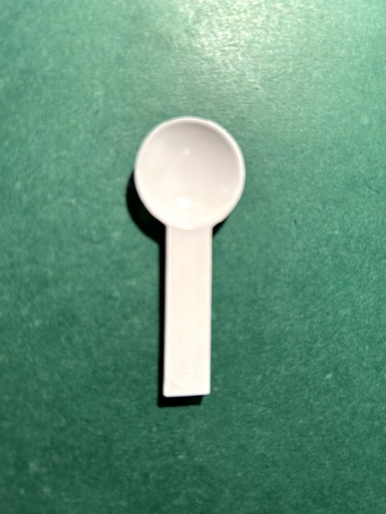 Witte plastic maatlepel op een groene achtergrond.
