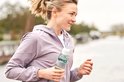 Vrouw in paars jack met een Mepal waterfles met witte dop en groene band tijdens het sporten.