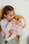 Een meisje geeft een baby-pop in roze kleding een flesje.