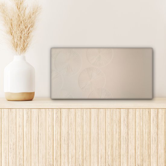 Beige canvas met cirkelvormige patronen, hangend boven een houten kast met een vaas met pampasgras.