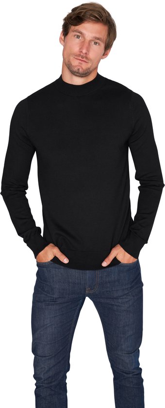 Man met zwarte coltrui en jeans, handen in de zakken.