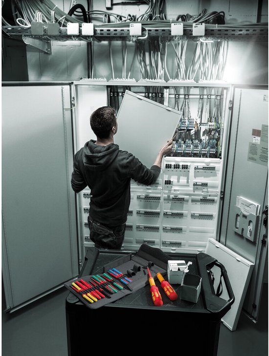 Een technicus plaatst een paneel in een schakelkast, met een gereedschapstas en schroevendraaiers op een werktafel.