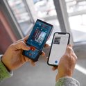 Handen die een Bosch laser afstandsmeter en een smartphone vasthouden, verbonden via Bluetooth.