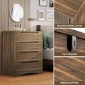 Commode marron à 4 tiroirs avec poignées découpées, à côté d'un miroir et d'un lit. Détails sur le coin arrondi et la protection anti-basculement.