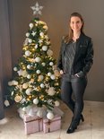 Vrouw in zwart kunstleren jack en glittertop bij kerstboom.