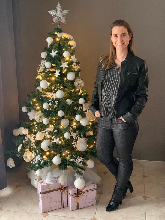 Vrouw in zwart kunstleren jack en glittertop bij kerstboom.