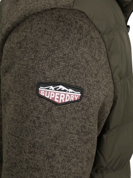 Detail van de gebreide linkermouw van een groene Superdry jas met een Superdry logo patch.