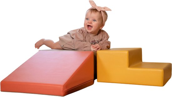 Een baby met strik ligt op een roze helling naast een geel trappetje.