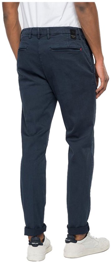 Achterkant man met donkerblauwe chino broek, omgeslagen broekspijpen en witte sneakers.