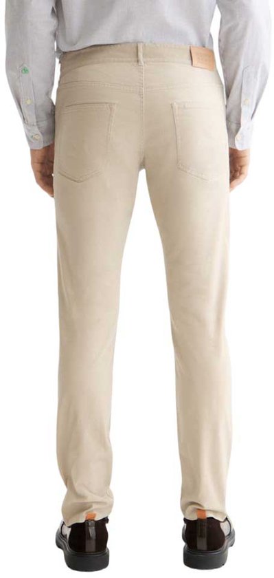 Achterkant van beige herenbroek op model, met leren label en twee zakken.