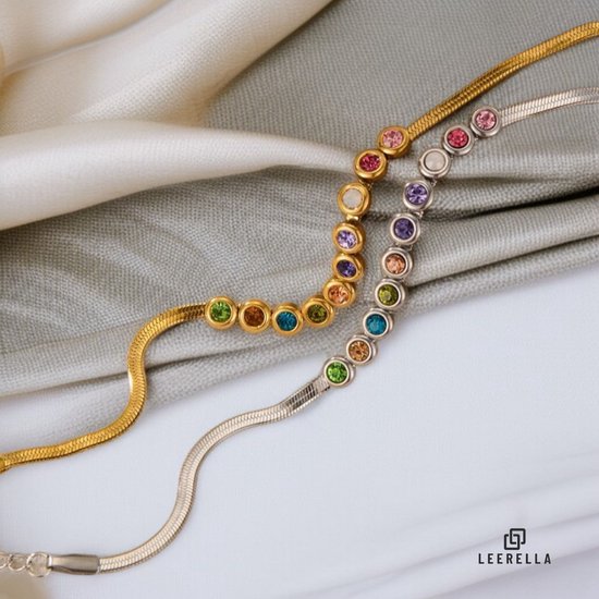 Goudkleurige en zilverkleurige armbanden met veelkleurige edelstenen, liggend op een zacht textiel.