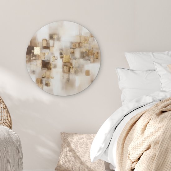 Abstracte muurcirkel met bruine en gouden vierkanten op een lichte achtergrond, boven een bed met beige sprei en kussens.