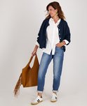 Model draagt een witte blouse, donkerblauwe gebreide cardigan, spijkerbroek en sneakers.