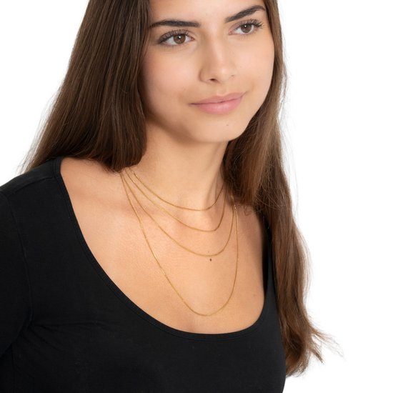 Gros plan d'une femme aux longs cheveux bruns portant plusieurs fines chaînes dorées.