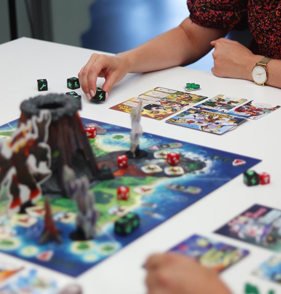 Een speler legt dobbelstenen op het bordspel 'King of Monster Island' met monsters en een vulkaan.
