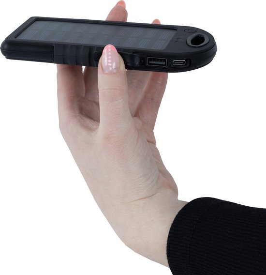 Hand met zwarte zonnepaneel powerbank, met USB- en USB-C-poorten zichtbaar.