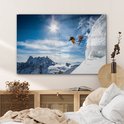 Een glasschilderij van twee skiërs die van een berg springen, hangend boven een bed.