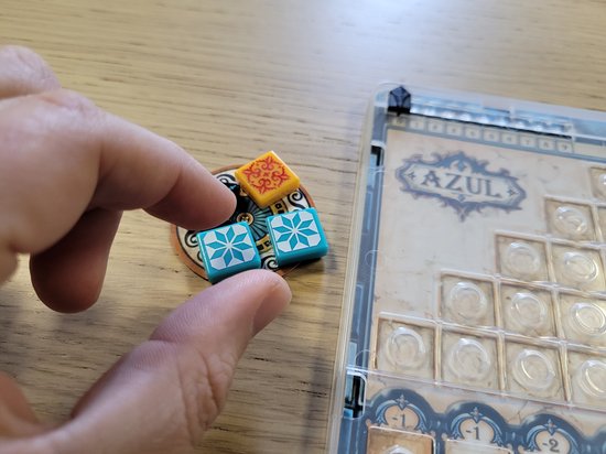 Hand neemt Azul Mini tegels met patronen van sterren en vierkanten.