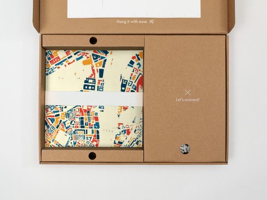 Une boîte en carton brun ouverte contenant une carte stylisée de bâtiments en bleu, orange et rouge sur fond crème.
