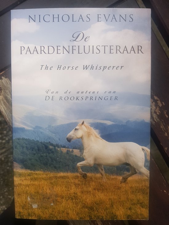 Boek 'De Paardenfluisteraar' met een witte paard in een veld met gouden gras en blauwe lucht.