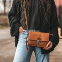 Een cognac leren schoudertas van The Chesterfield Brand, gedragen door een model met blauwe jeans en een zwarte fluffy jas.
