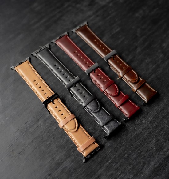 Vier leren Apple Watch bandjes in de kleuren bruin, zwart, rood en donkerbruin, liggend op een donkere ondergrond.