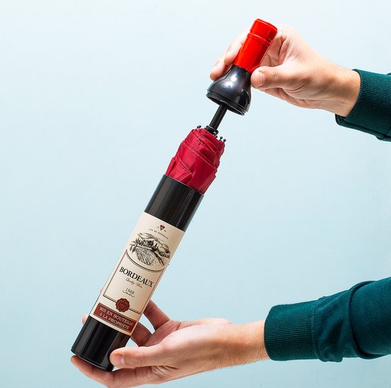 Opvouwbare rode paraplu, opgevouwen in een zwarte fles met Bordeaux wijnlabel, rode dop.
