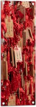 Tuinposter – Rode Sleutelhangers met Chinese Tekens aan een Muur - 30x90 cm Foto op Tuinposter (wanddecoratie voor buiten en binnen)
