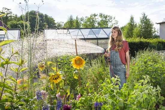Een vrouw met tuinbroek sproeit met een grijze GARDENA spuit met oranje accenten.