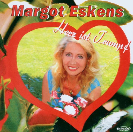 Margot Eskens lacht, met rode hartvormige kader, blauw topje, en bloemen.