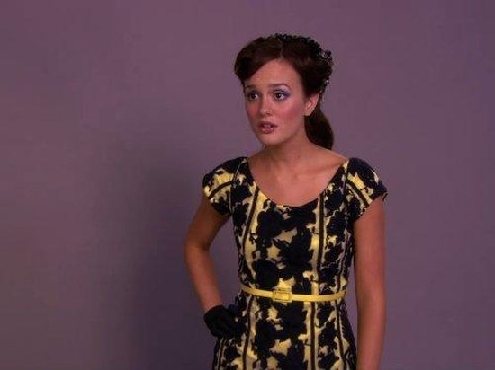 Vrouw met bruin haar in een jurk met gele riem en zwarte handschoenen.