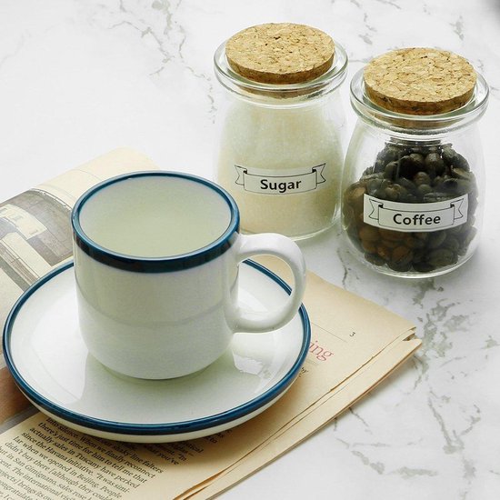 Wit koffiekopje met blauwe rand op een schotel, naast twee glazen potten met deksel.