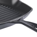 Detail van een zwarte gietijzeren grillpan met ribbels en een handvat met Le Creuset-logo.