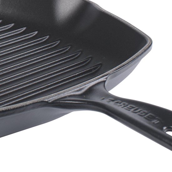 Detail van een zwarte gietijzeren grillpan met ribbels en een handvat met Le Creuset-logo.