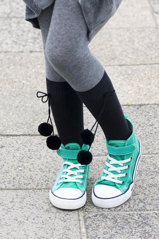 Kind draagt grijze panty met zwarte kniekousen met pompons en turquoise sneakers met witte veters.