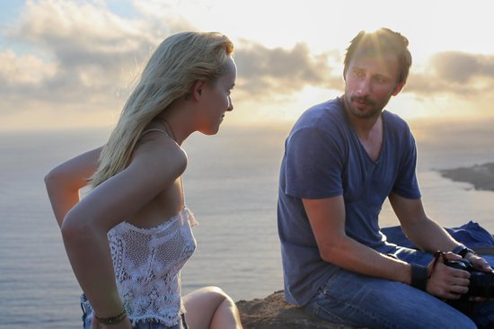Man en vrouw op een rots, de zon gaat onder. Vrouw met blond haar draagt een wit kanten topje, man met blauw T-shirt.