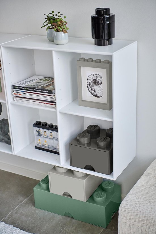 Witte wandkast gevuld met tijdschriften, een fotolijst en LEGO opbergdozen in grijs en groen.