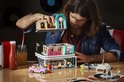 Man bouwt LEGO diner op tafel met roze auto, sap en stapels vinylplaten.
