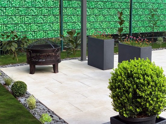 Gardebruk vuurkorf op een betegeld terras met groen gras en planten.