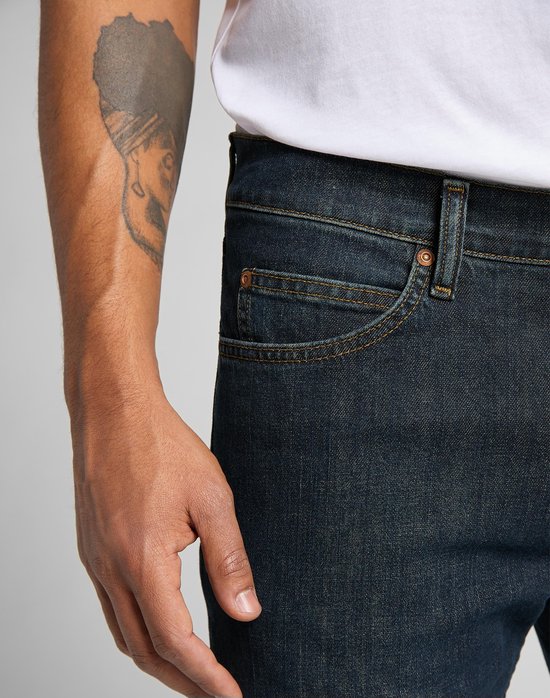 Detail van de donkerblauwe Lee jeans, voorvak met klinknagel en bruine stiksels.