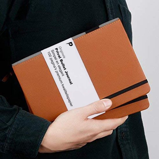 Een bruine bullet journal in een hand. "Originele Prival Bullet Journal Simpel en elegant 100 pagina's premium kwaliteispapier."