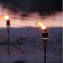 Twee brandende bamboe fakkels op een zanderige ondergrond bij zonsondergang.