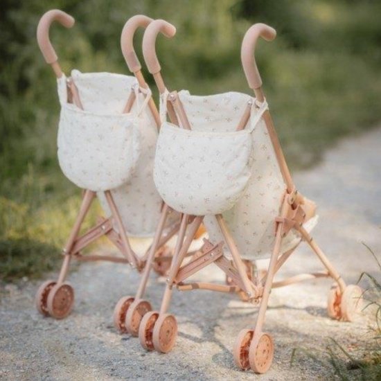 Twee roze poppenbuggy's met wit textiel met bloemenpatroon, staand op een kiezelpad.