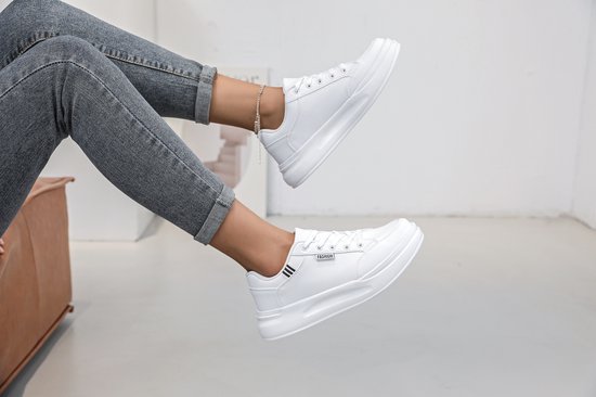 Voeten in witte lage sneakers met veters, de ene voet omhoog.