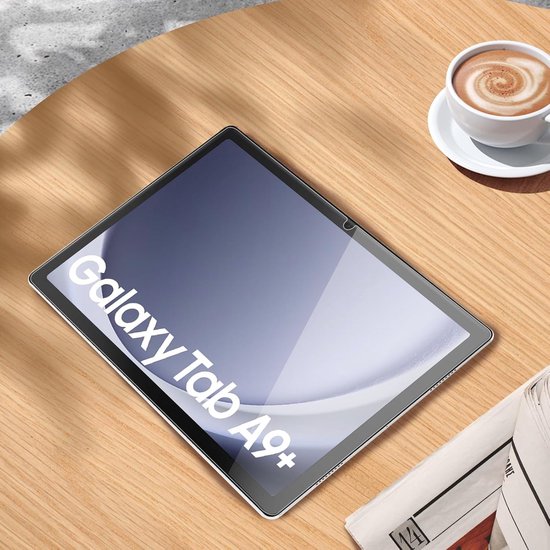 Samsung Galaxy Tab A9+ met een kopje koffie en krant op een houten tafel.